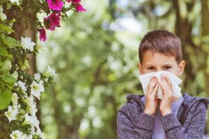 Photo of young boy near flowers holding tissue to nose and scowling from "9 Recipes To Treat Seasonal Allergies Naturally With Food" by Green Smoothie Girl