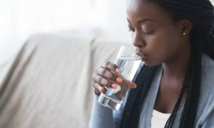 Photo of African American woman with long hair sitting on couch and drinking clear water from "How Do I Prepare For a 3-Day Modified Fast?" blog post by Green Smoothie Girl