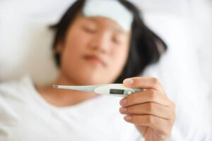 Photo of Korean woman with white towel on forehead and holding a thermometer from "The Science Behind Sauna’s Effect On Your Immune System" blog post by Green Smoothie Girl