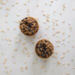 Photo of two oatmeal blueberry muffins top-view with raw oatmeal scattered on white surface from "Oatmeal Blueberry Muffins" recipe by Green Smoothie Girl
