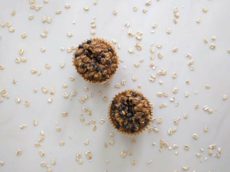 Photo of two oatmeal blueberry muffins top-view with raw oatmeal scattered on white surface from "Oatmeal Blueberry Muffins" recipe by Green Smoothie Girl