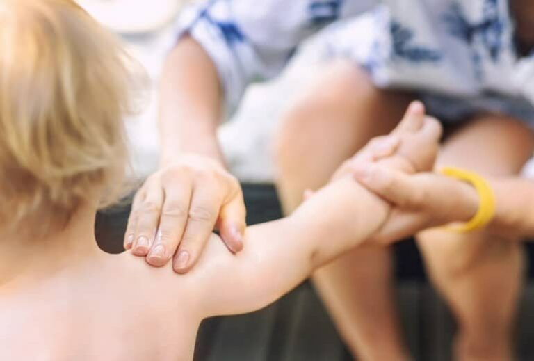 Photo of a women rubbing sunscreen into a blond child's arm from Green Smoothie Girls' The Ultimate Guide to Reading Sunscreen Labels