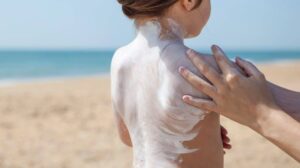 A child on the beach having sunscreen rubbed on their back by an adult.