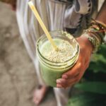 woman holding a green smoothie with a yellow straw in a jar