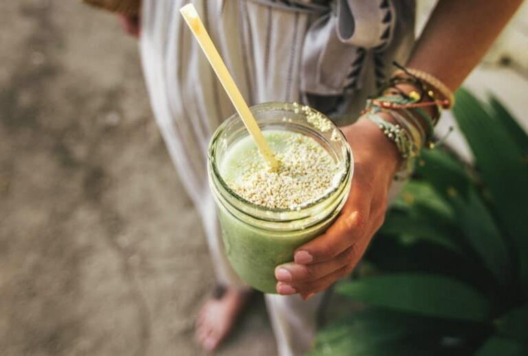 woman holding a green smoothie with a yellow straw in a jar