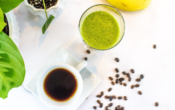 A cup of coffee next to a glass of green smoothie with coffee beans scattered around from Green Smoothie Girl's "Wake Up! Green Smoothie"
