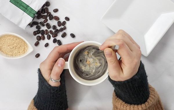 a woman's hands stirring coffee in a white mug . There are coffee beans on the table from Green Smoothie Girl's "Immune-Boosting Bone Broth Coffee Elixir"