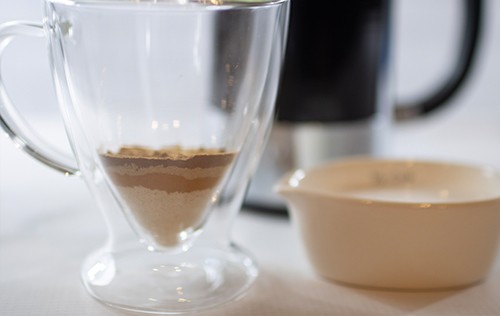 two drinking glasses, one filled with brown powder, and the other with liquid from Green Smoothie Girl's "Inflammation Fighting, High-Protein Turmeric Coffee"