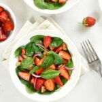 image of a bowl of spinach and strawberries with several bowls of individual strawberries surrounding it from Green Smoothie Girl's "spinach strawberry salad" recipe