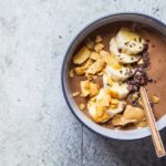 image of a white bowl containing brown smoothie and sliced banana topped with sprinkled chocolate from Green Smoothie Girl's recipe "coffee acai bowl"
