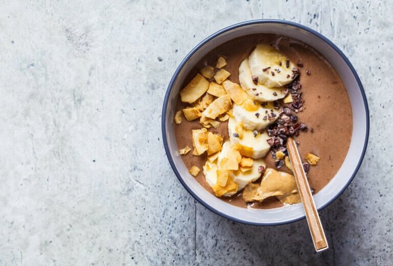 image of a white bowl containing brown smoothie and sliced banana topped with sprinkled chocolate from Green Smoothie Girl's recipe "coffee acai bowl"