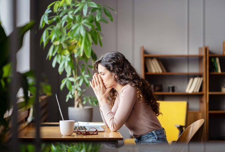 The profile of a woman facing left while sitting at a desk and looking at her open laptop