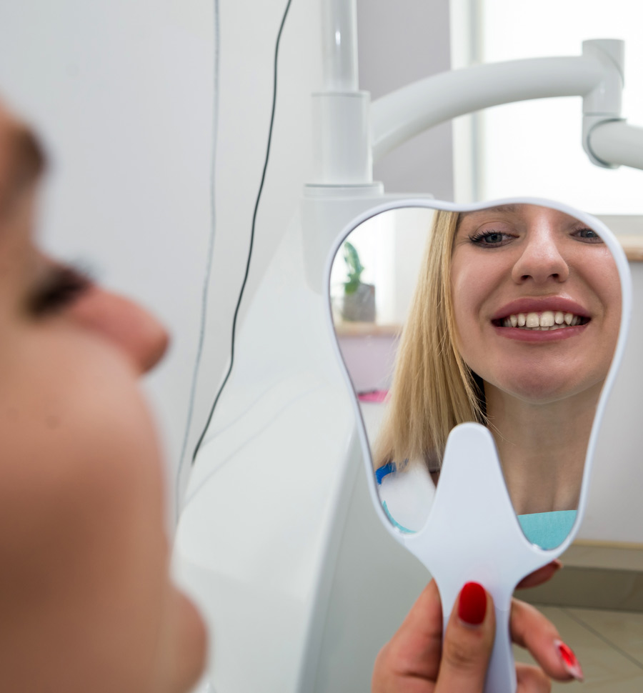 Woman at the dentist looking at her teeth in a mirror that is shaped like a tooth