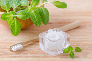 alternative natural toothpaste coconut oil and wood toothbrush closeup mint on wooden background